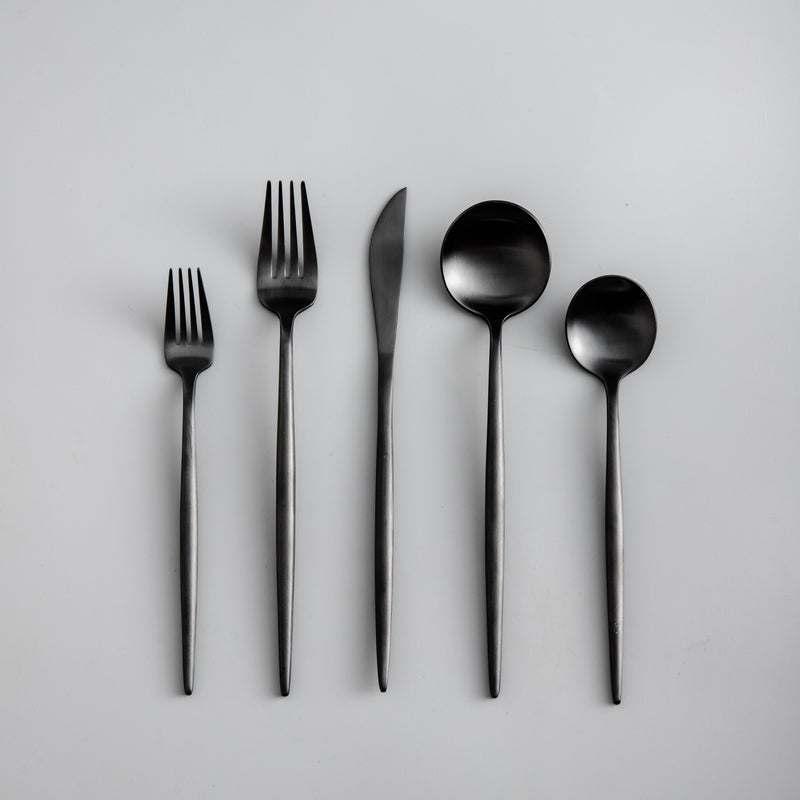 Anordnung eines modernen Bestecksets in Schwarz auf einem Geschirrteller.