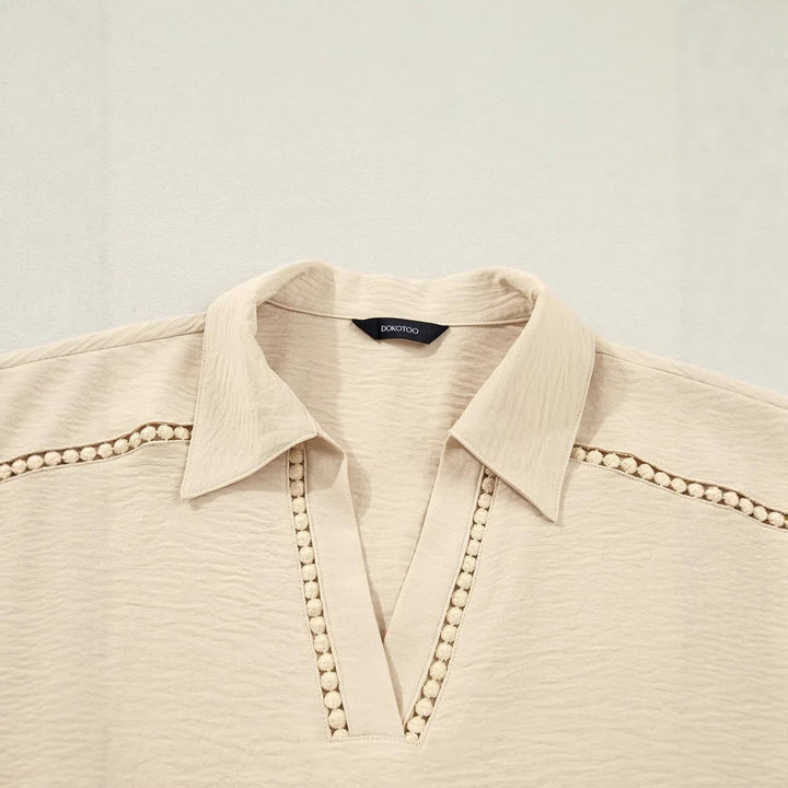 Weiße Frauenbluse mit floraler Spitze, tiefem V-Ausschnitt und hochkrempelbaren Ärmeln. Vielseitig kombinierbar.