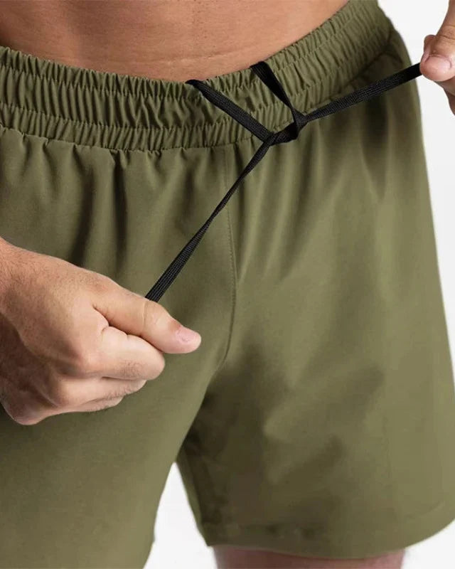 Mann trägt schnelltrocknende Herren Sportshorts beim dynamischen Fitness-Training. Ergonomischer Schnitt.