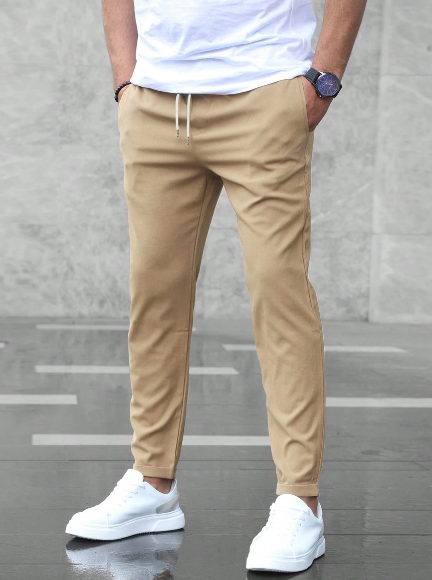 Stylisches Herren Outfit: schwarze Slim Fit Hose mit Tunnelzug, weißes T-Shirt, Sneaker, moderner Freizeit-Look.