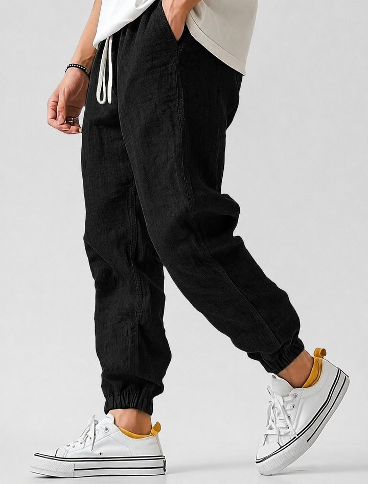 Mann trägt bequeme Herren Sommer Jogger entspannt im Park. Ideal als leichte Freizeithose für Frühling & Sommer.