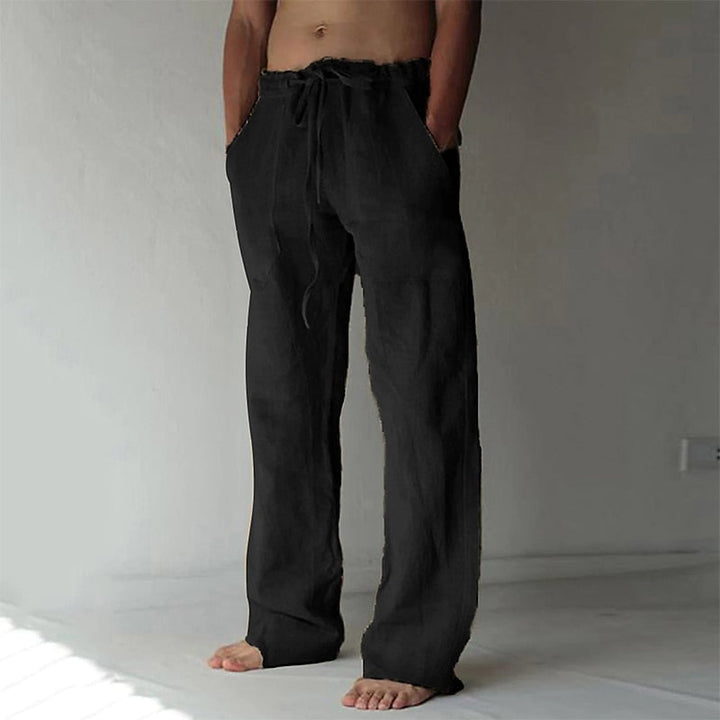 Mann trägt lockere Leinenhose Elias am Strand, weiter Schnitt, ideal für entspannte Sommertage.