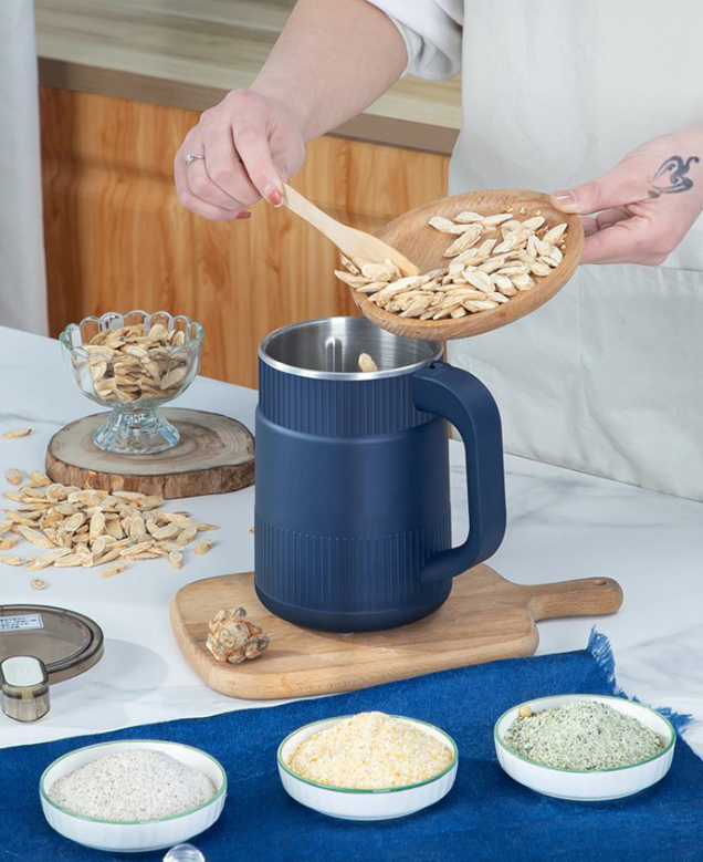Elektrische Getreidemühle umgeben von verschiedenen Körnern, Kaffeebohnen und Saaten.