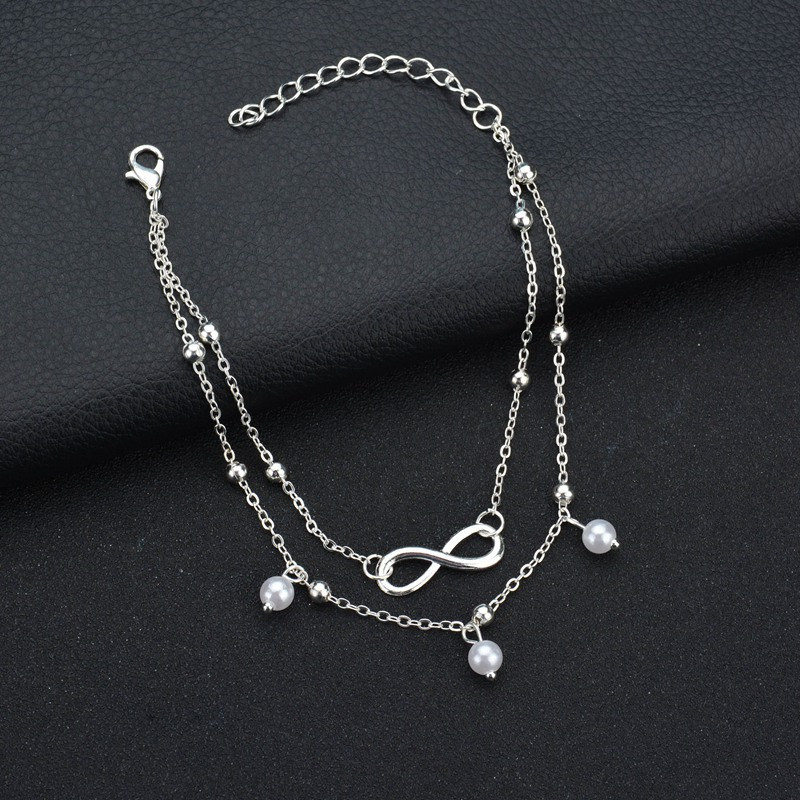 Frauen-Knöchelarmband mit glänzenden Retro-Perlen und filigranem Unendlichkeits-Anhänger. Modisches Schmuckstück.