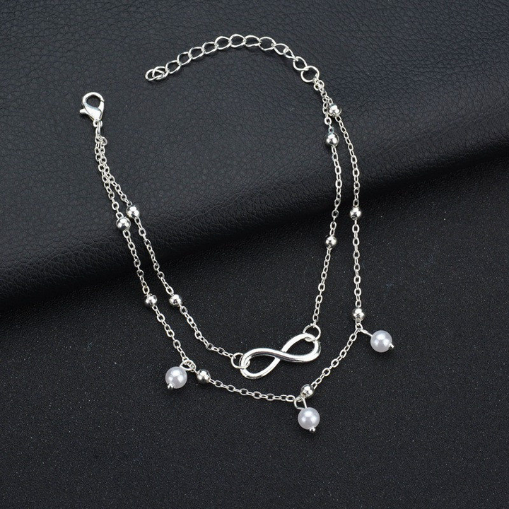 Frauen-Knöchelarmband mit glänzenden Retro-Perlen und filigranem Unendlichkeits-Anhänger. Modisches Schmuckstück.