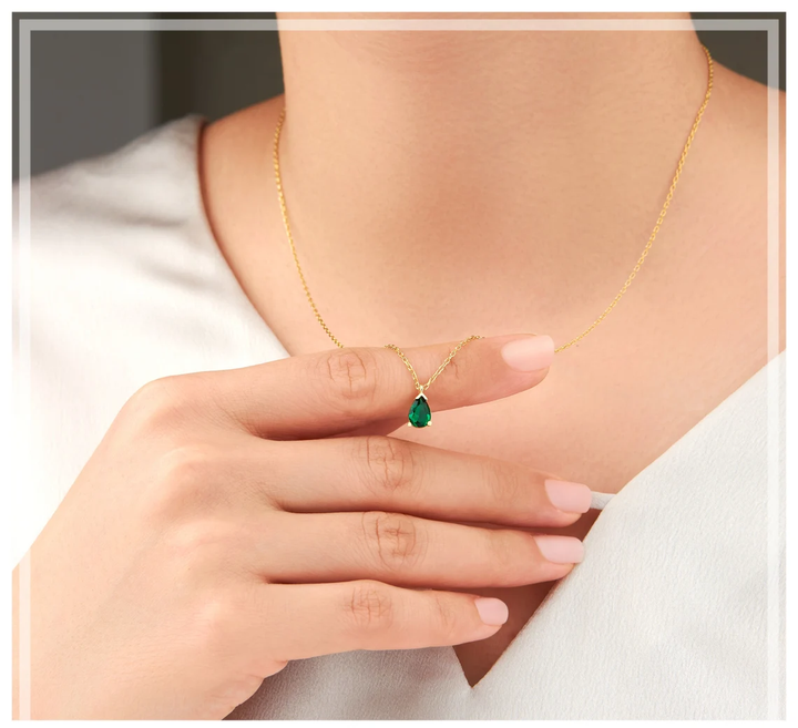 Elegante goldfarbene Damen-Halskette mit funkelndem Smaragd-Tropfen-Anhänger, ideal für besondere Anlässe.